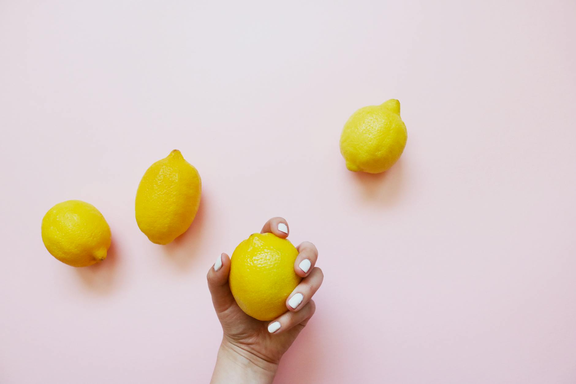 Hand holding a fresh lemon on a soft pink background, symbolizing renewed vitality and natural pleasure