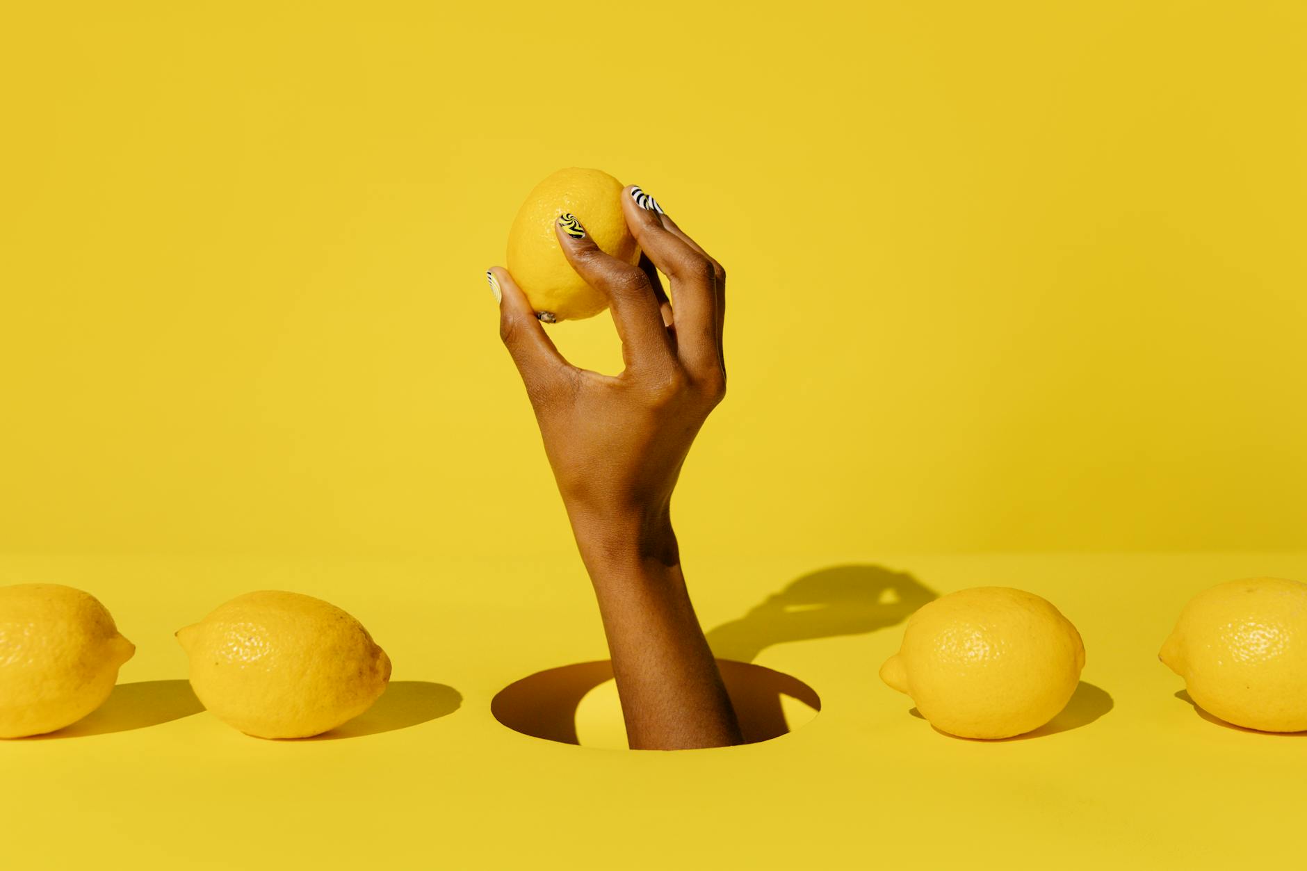 A hand holding a bright yellow lemon against a vivid yellow background, symbolizing fresh starts and rebuilding desire