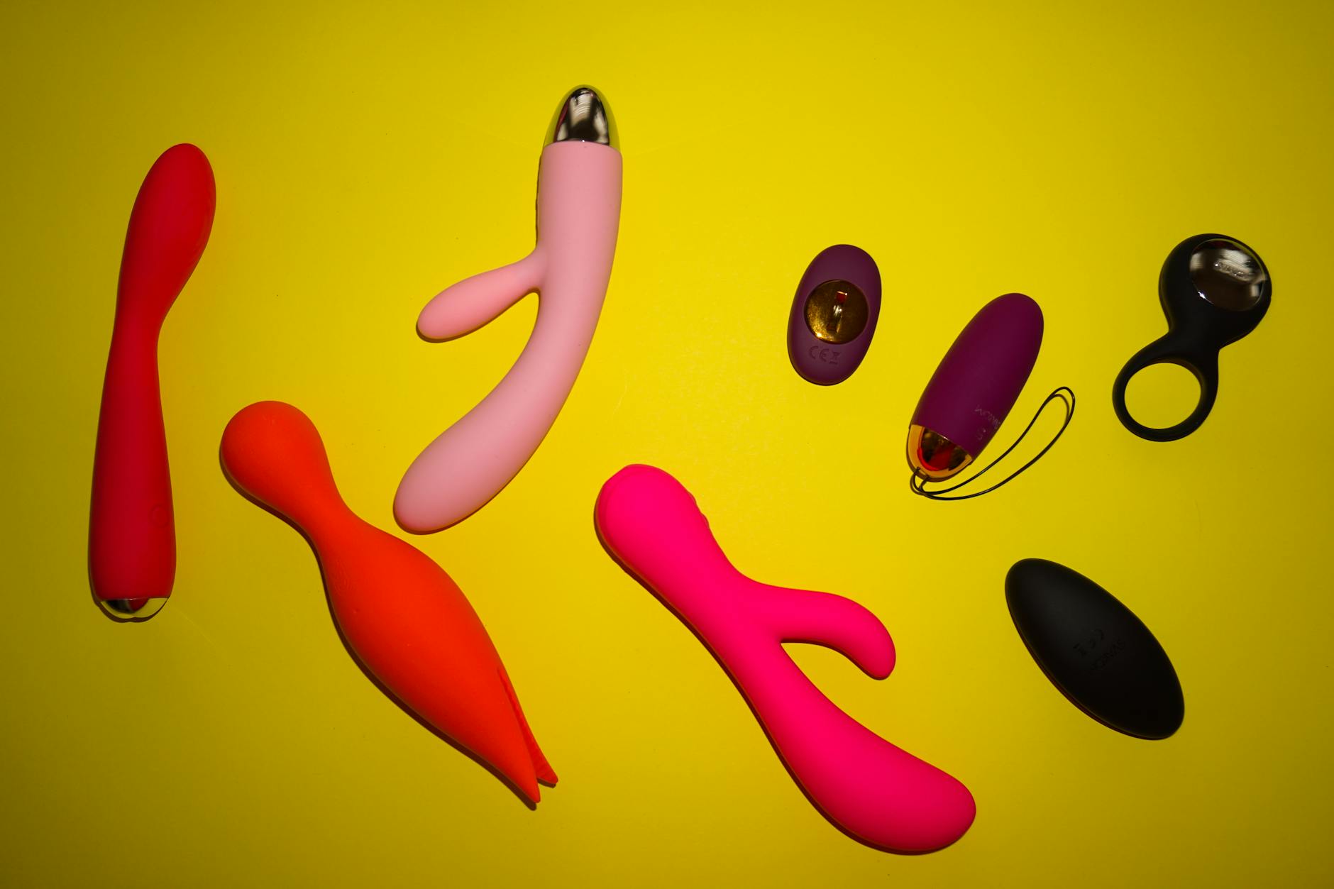 Colorful vibrators arranged on a bright yellow surface, representing diverse pleasure options