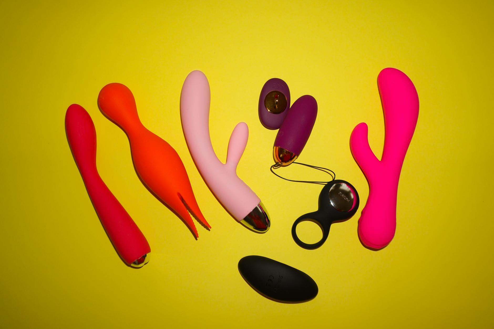 Colorful clitoral vibrators displayed on a bright yellow background, showcasing various pleasure devices